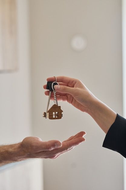 Manos entregando llaves de casa con llavero en forma de hogar - el momento de recibir las llaves de tu nuevo hogar